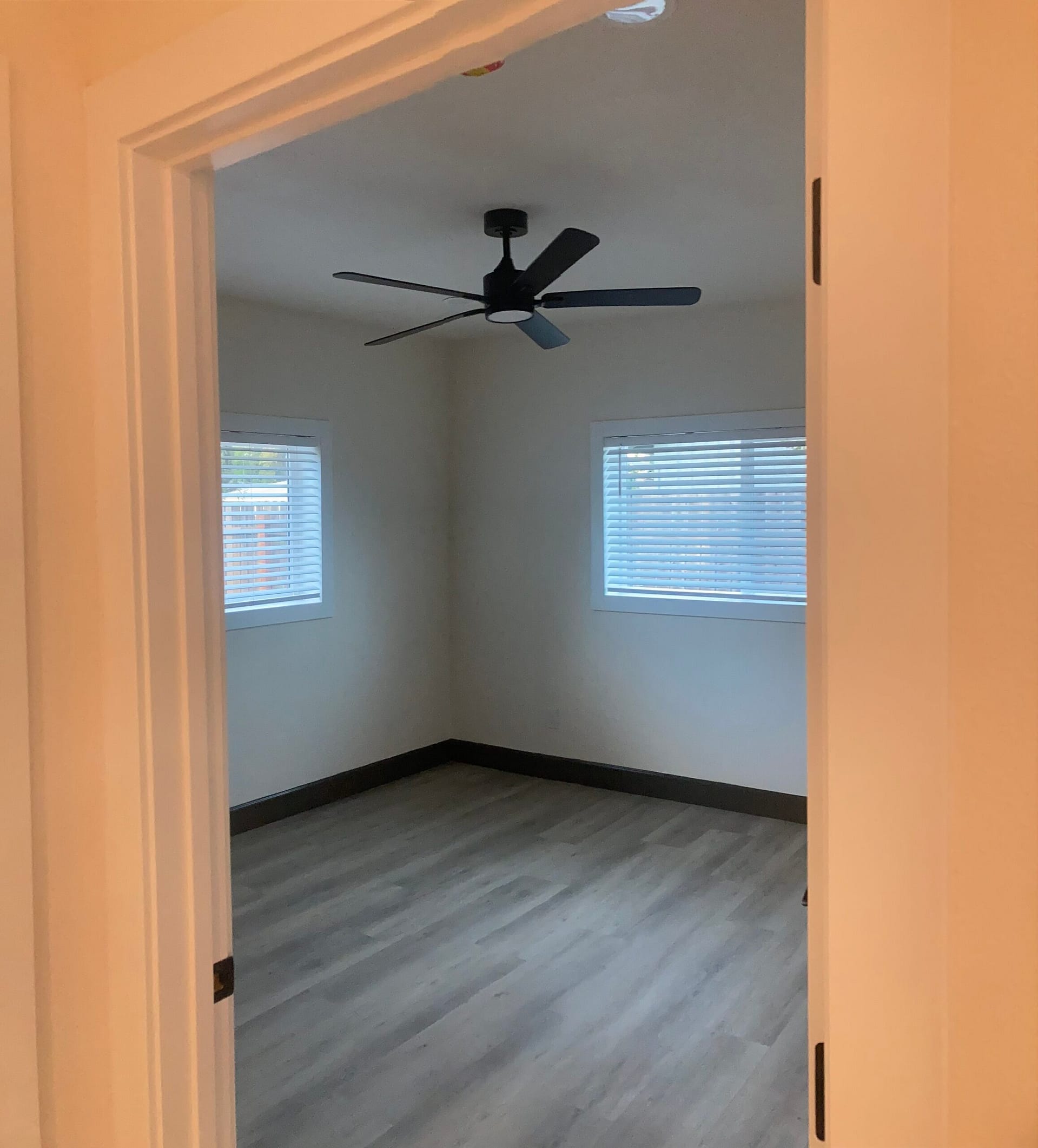 Finished room in a Redding garage conversion with a black ceiling fan, white window blinds and wood-look plank flooring.
