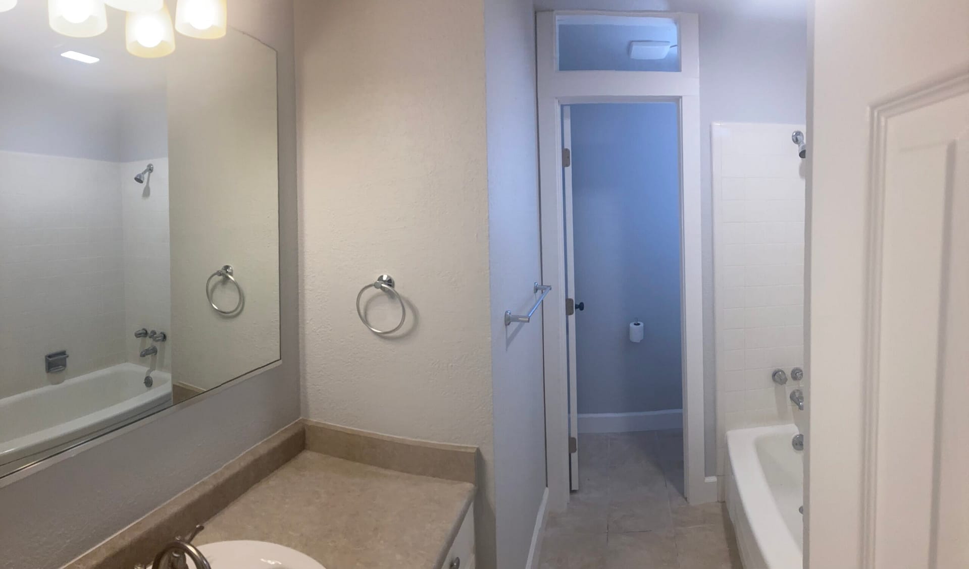 Bathroom with broad vanity mirror, countertop, towel rings and bathtub beside a white interior door.