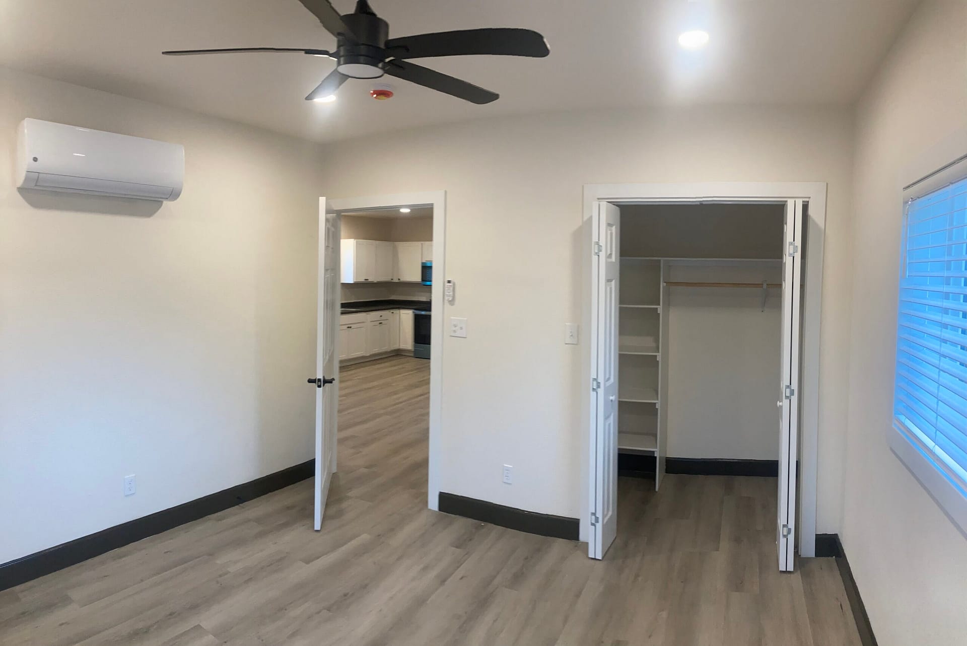 Finished ADU bedroom in Redding, CA, with wall-mounted ductless mini-split air conditioner, ceiling fan, walk-in closet and wood-look flooring.