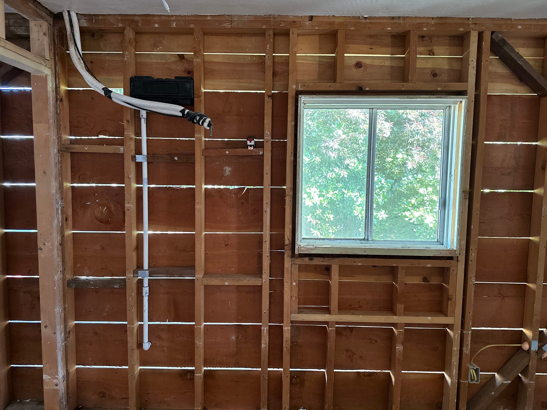 Exposed wood framing surrounding an existing window with wall cavities open and electrical lines visible.