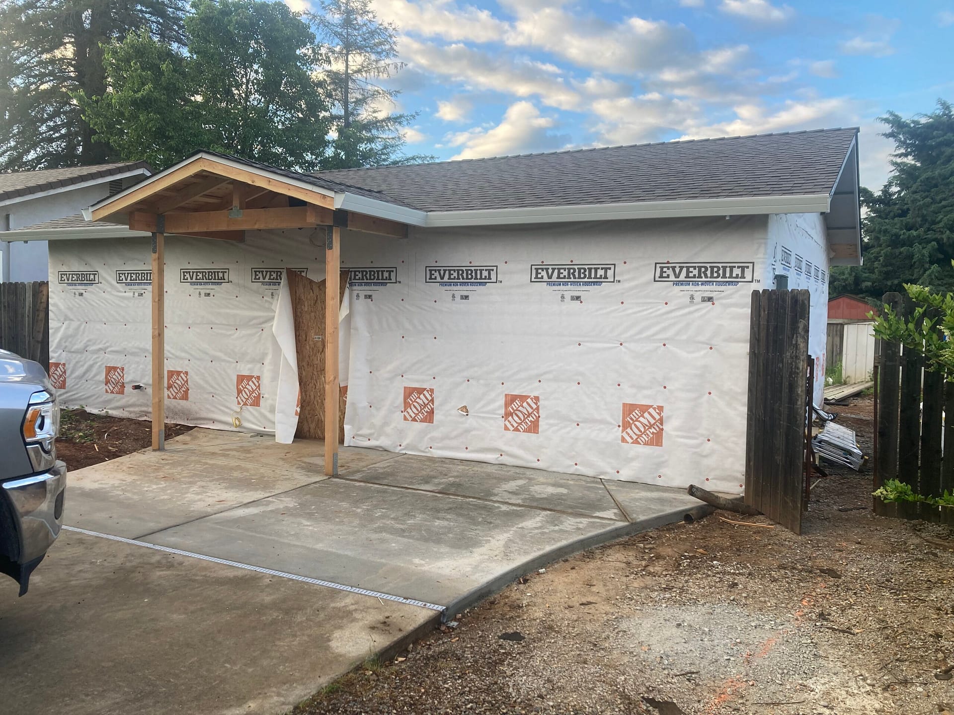 Residential siding installation preparation with house wrap, exterior weather barrier, covered entry porch framing, and concrete walkway.