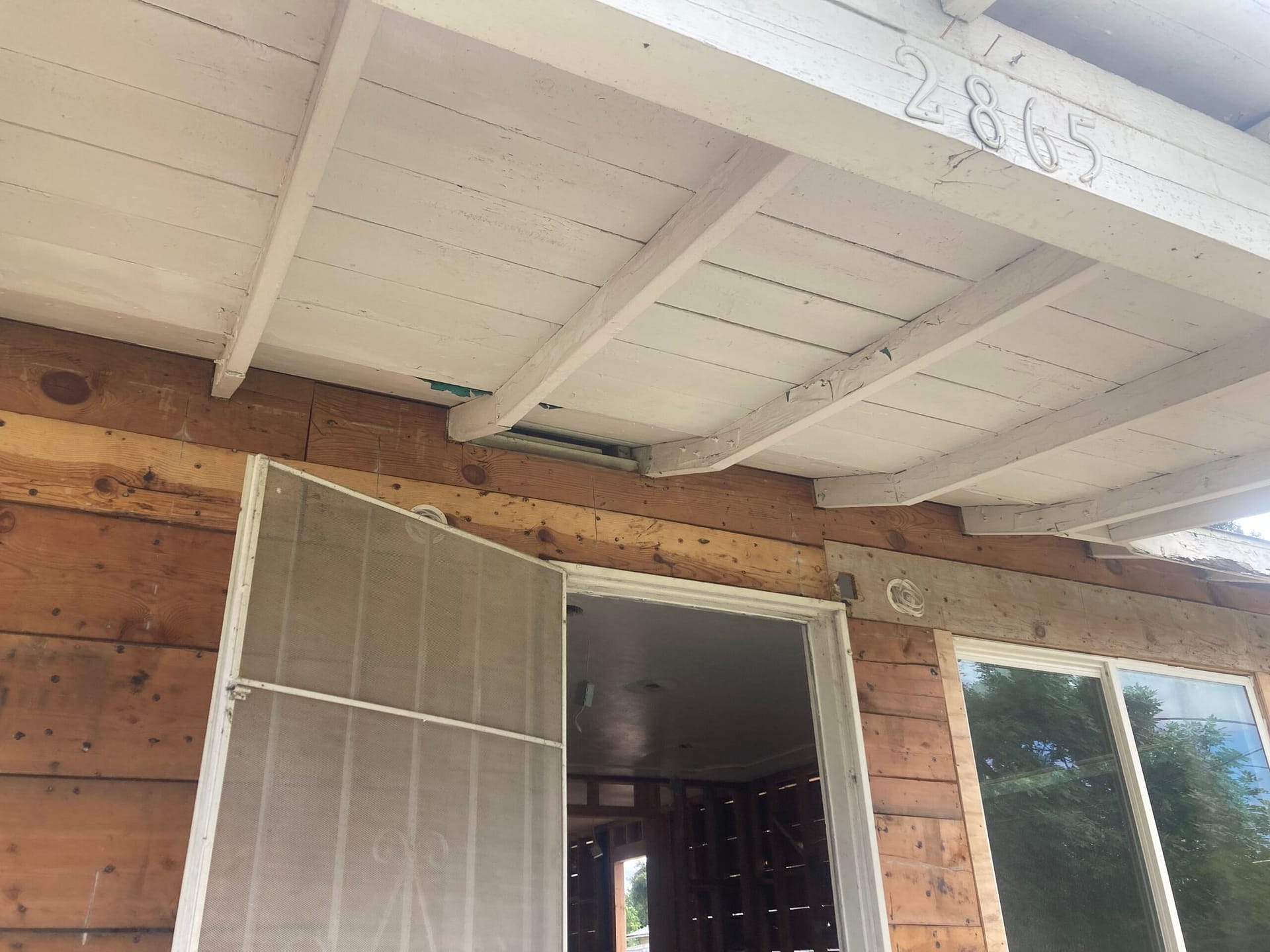 Exposed wood exterior wall beneath a painted porch roof with visible beams and rafters during renovation.