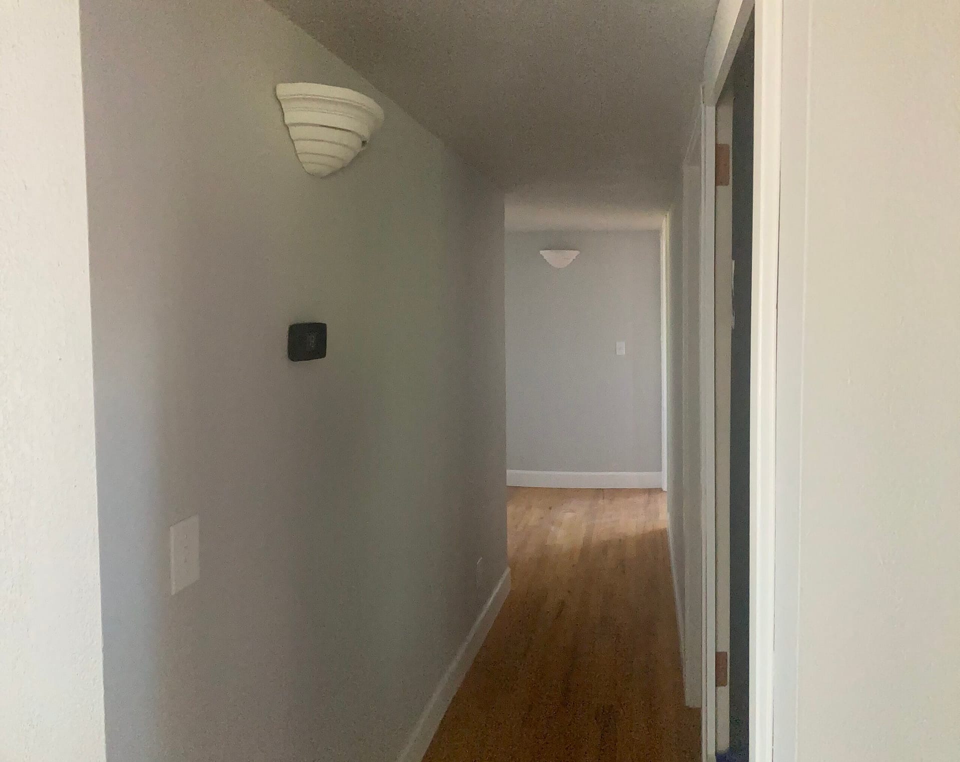 Long residential hallway with gray painted walls, wall sconces, white door trim and wood-look plank flooring.