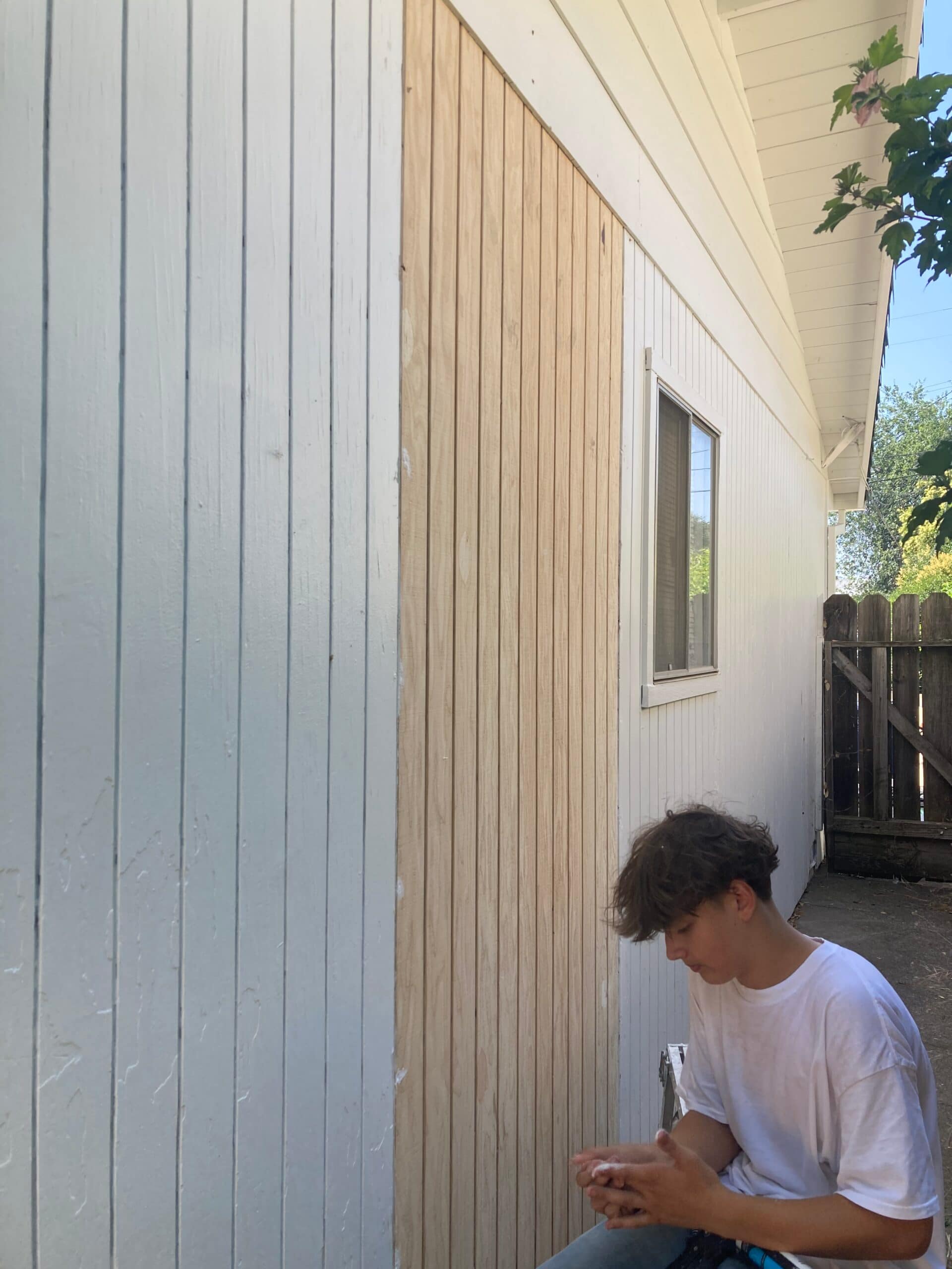 Exterior home wall with newly installed vertical wood siding boards beneath the eaves beside an existing window.