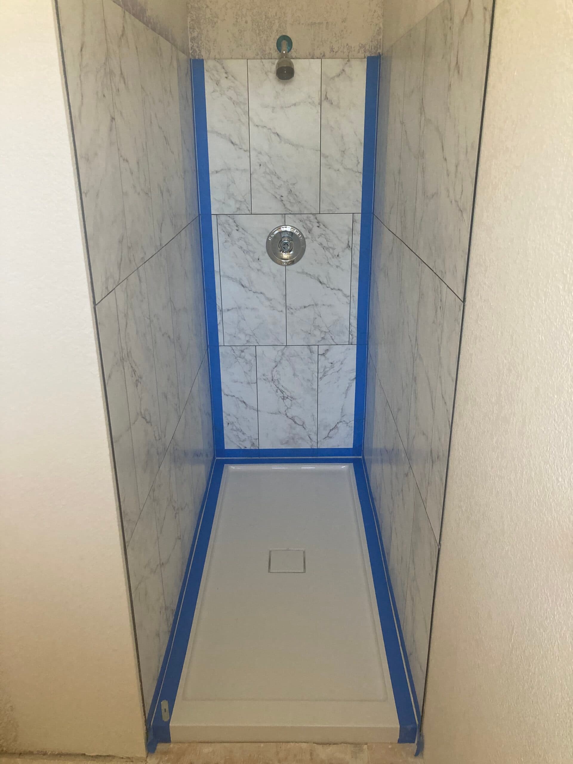 Shower remodel with marble-look wall tile, a new shower pan, and installed shower fixture in a residential bathroom.