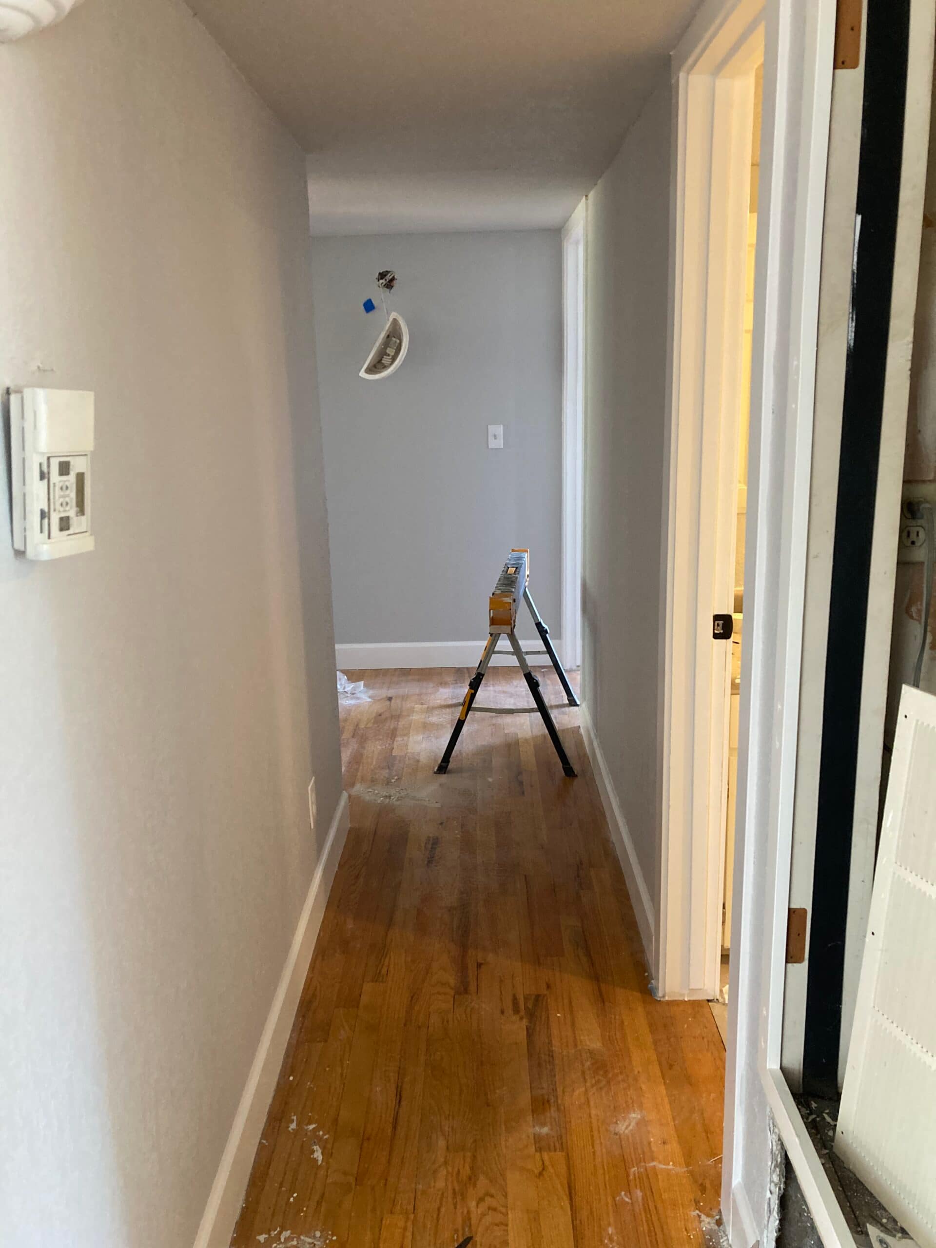 Interior hallway with wood-look flooring, light gray painted walls, white door trim and ladder during renovation.
