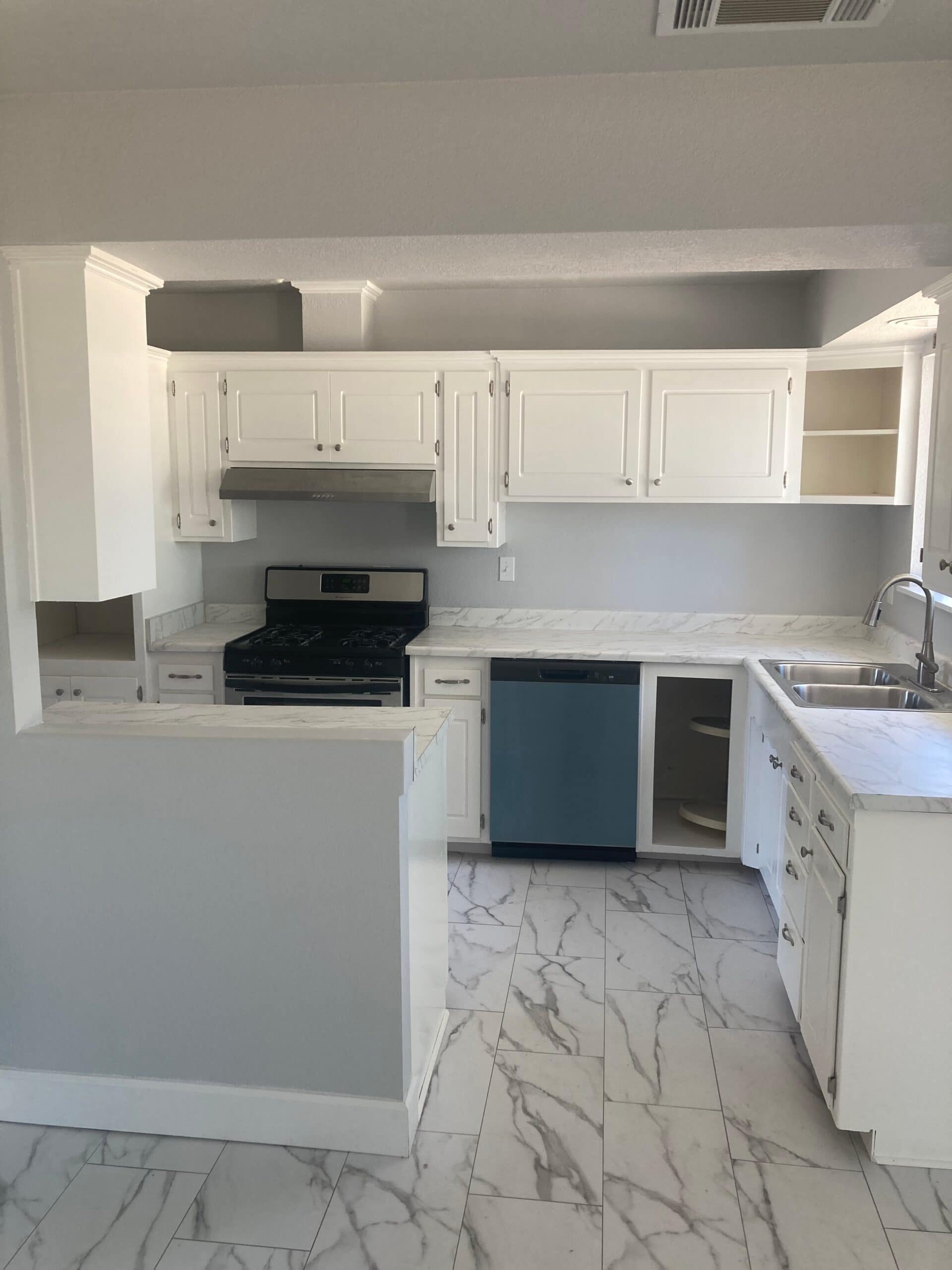 White kitchen cabinets, stove and sink seen over a breakfast bar with marble-look floor tile in adjoining space.