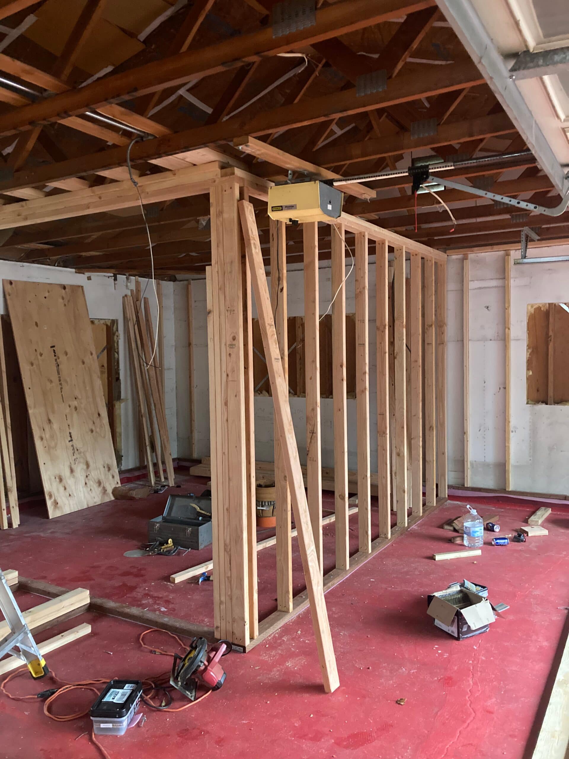 Newly assembled stud partition wall inside a garage with exposed roof trusses, bracing and construction tools.
