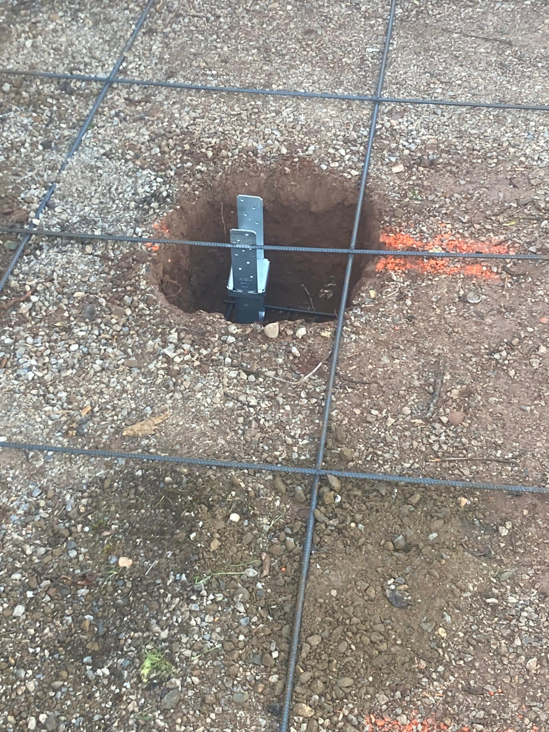Excavated hole for concrete footing installation during residential patio construction by On Point Construction.