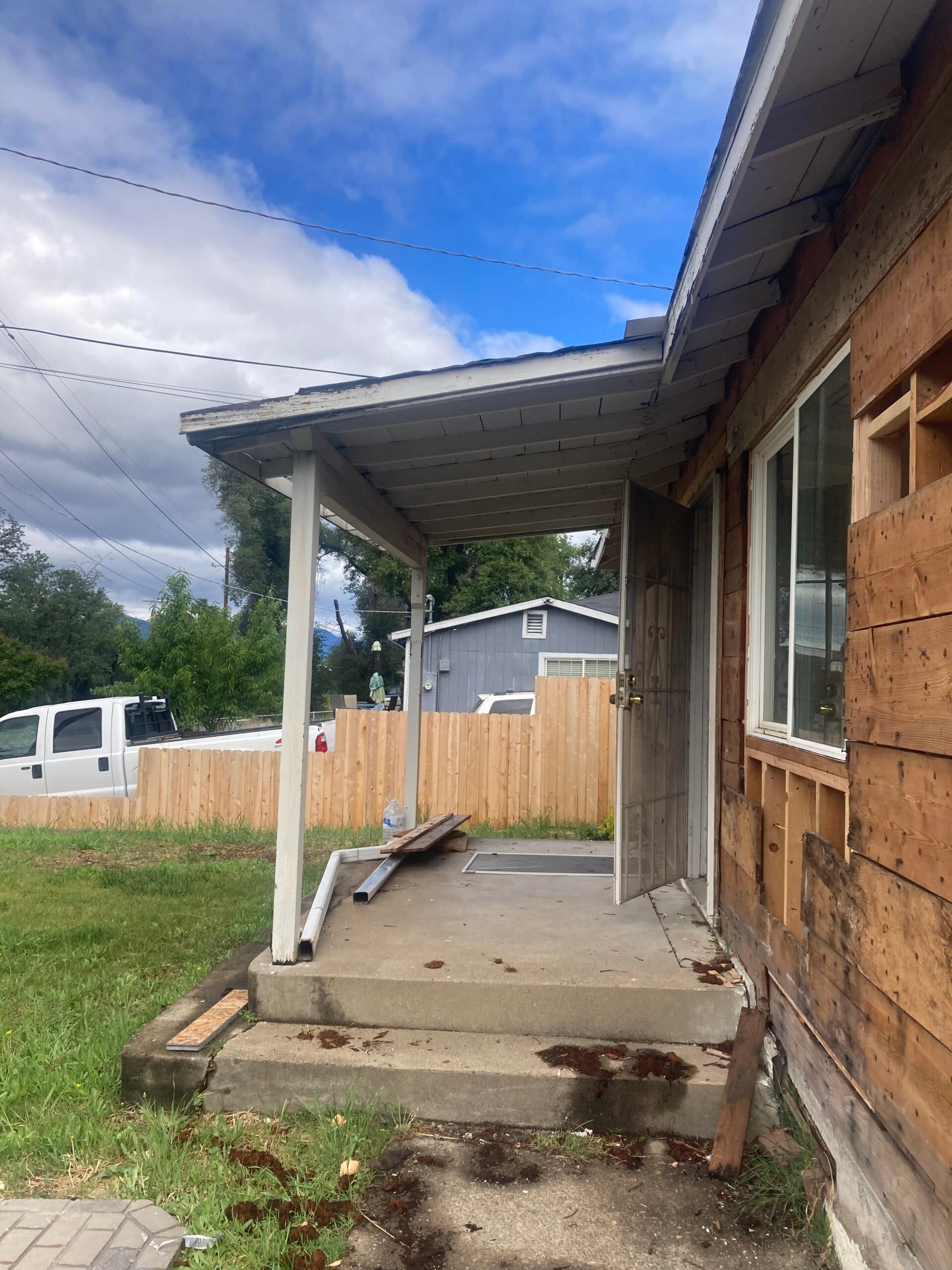 Home exterior during dry rot repairs, with house wrap over repaired walls, boarded door and window openings, and a new wood-framed porch cover.
