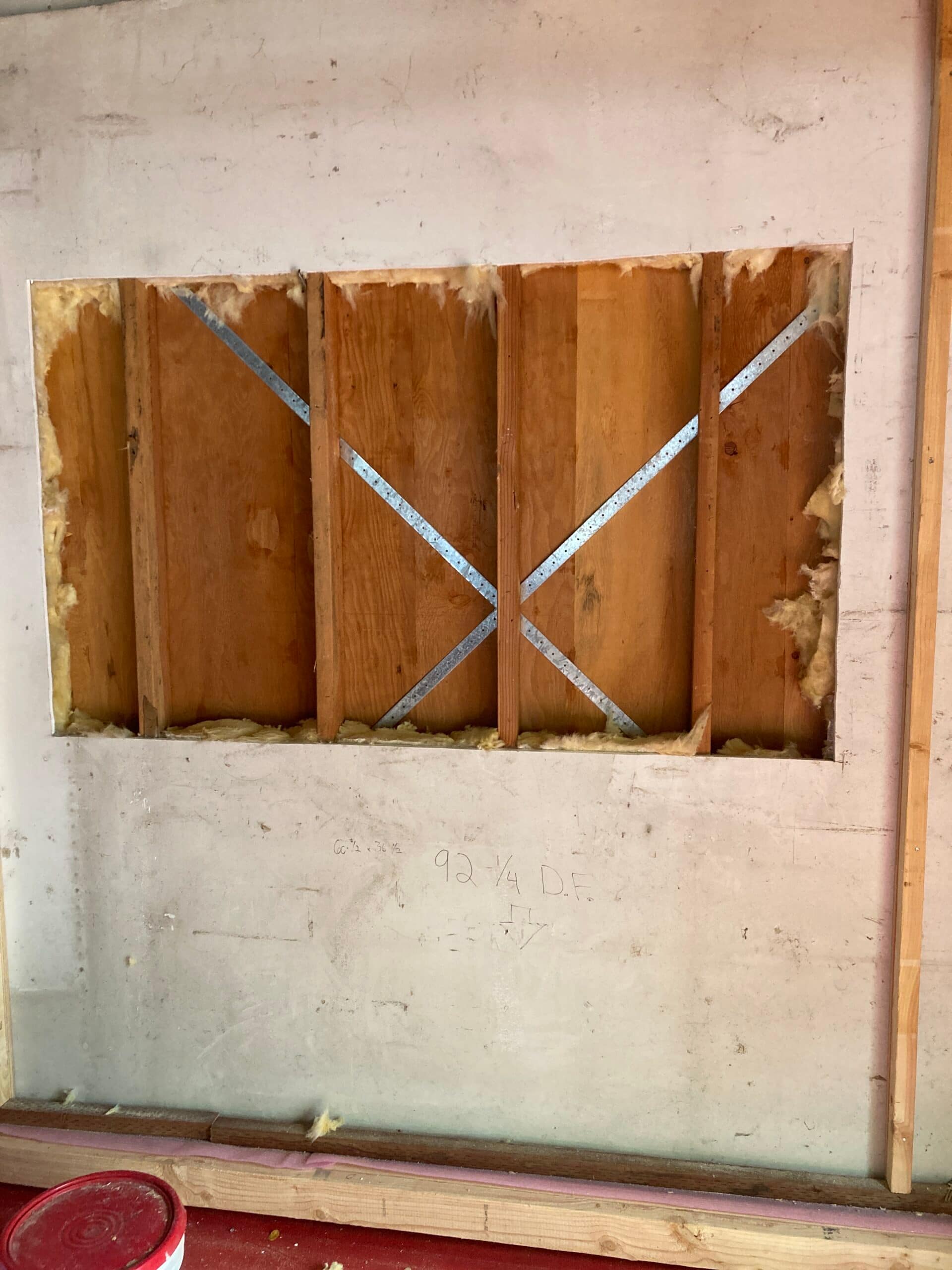 Rectangular opening cut in an interior wall exposing wood studs and diagonal metal braces during renovation.