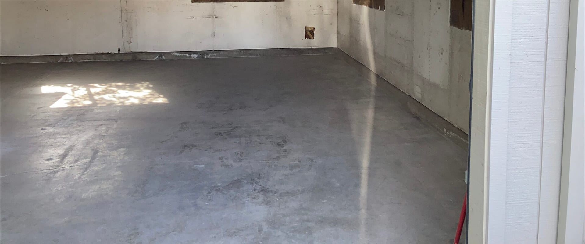 Bare concrete floor inside an unfinished garage or outbuilding with windows and walls exposed before construction.
