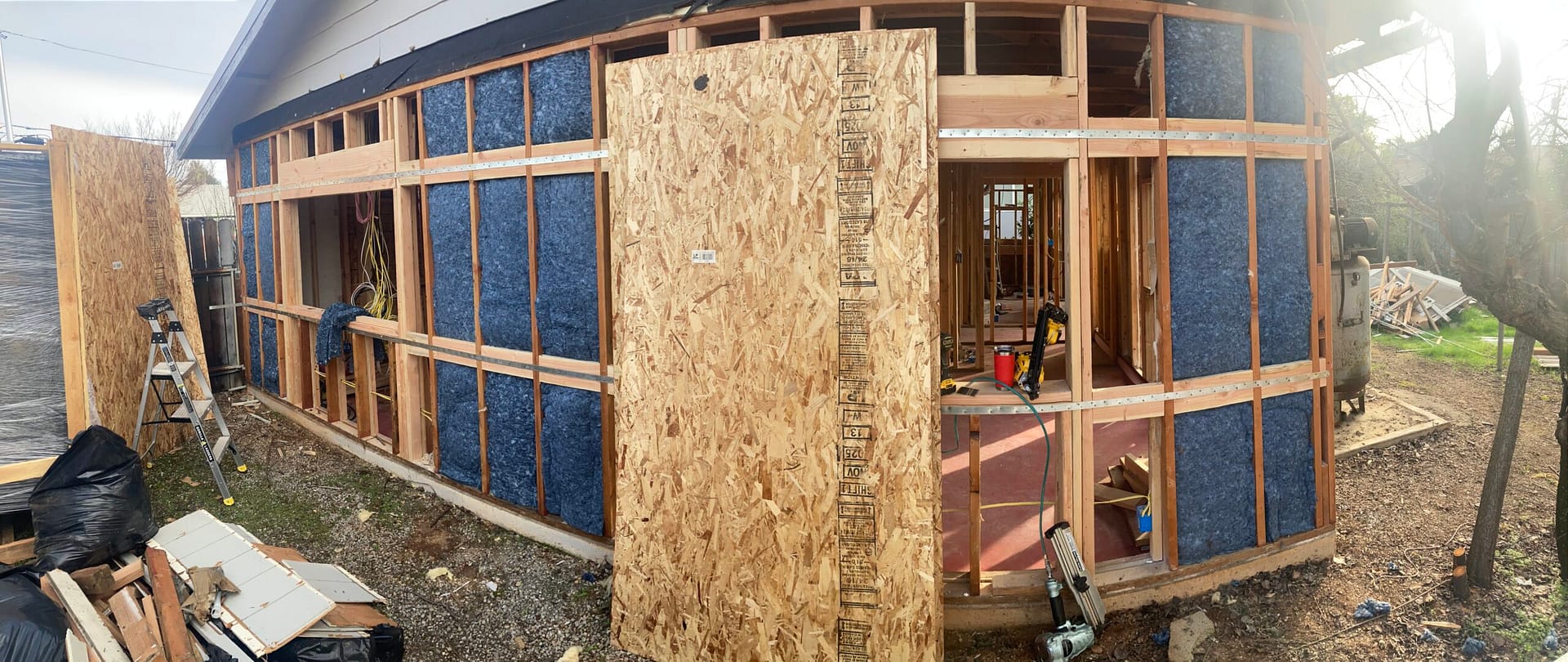 Exterior wall sheathing and siding installation in progress, showing exposed wood framing, wall insulation, and OSB panels by On Point Construction.