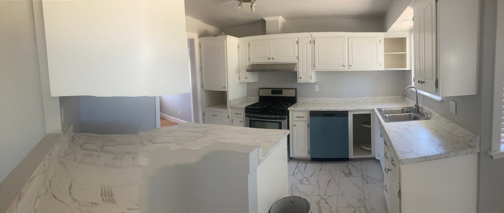 Remodeled kitchen with white shaker cabinets, large marble-look floor tiles, light countertops, dark range and kitchen sink.