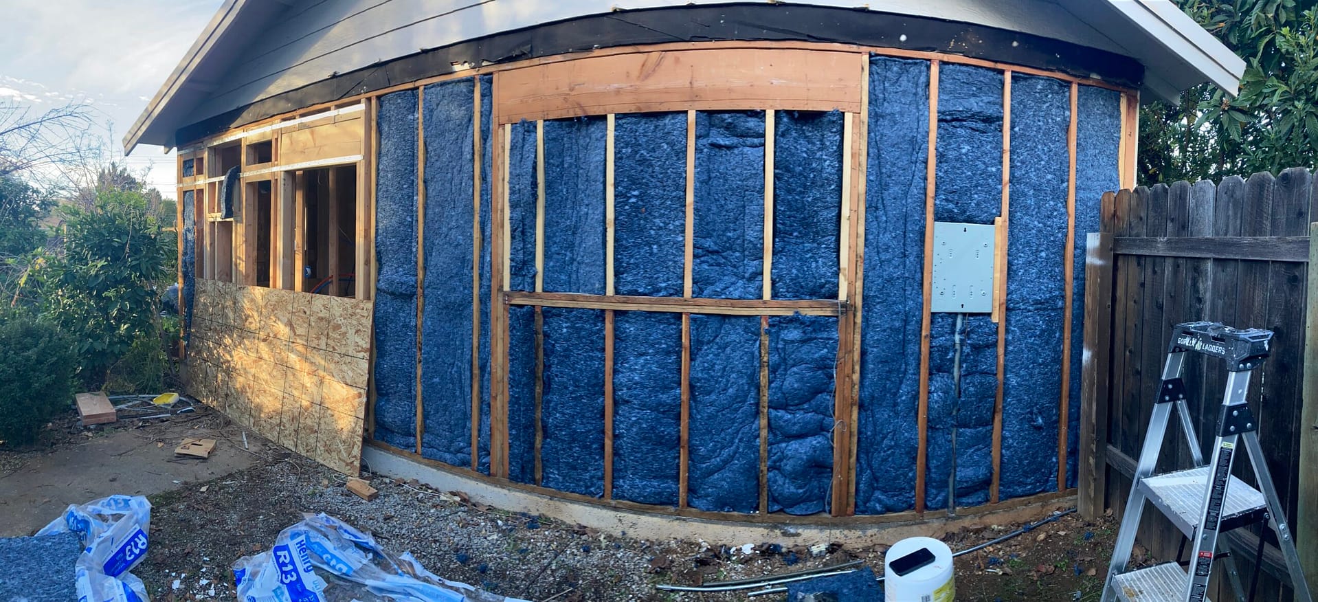 Exterior building wall with open wood framing, dark insulation panels and partial plywood sheathing before exterior finishes.