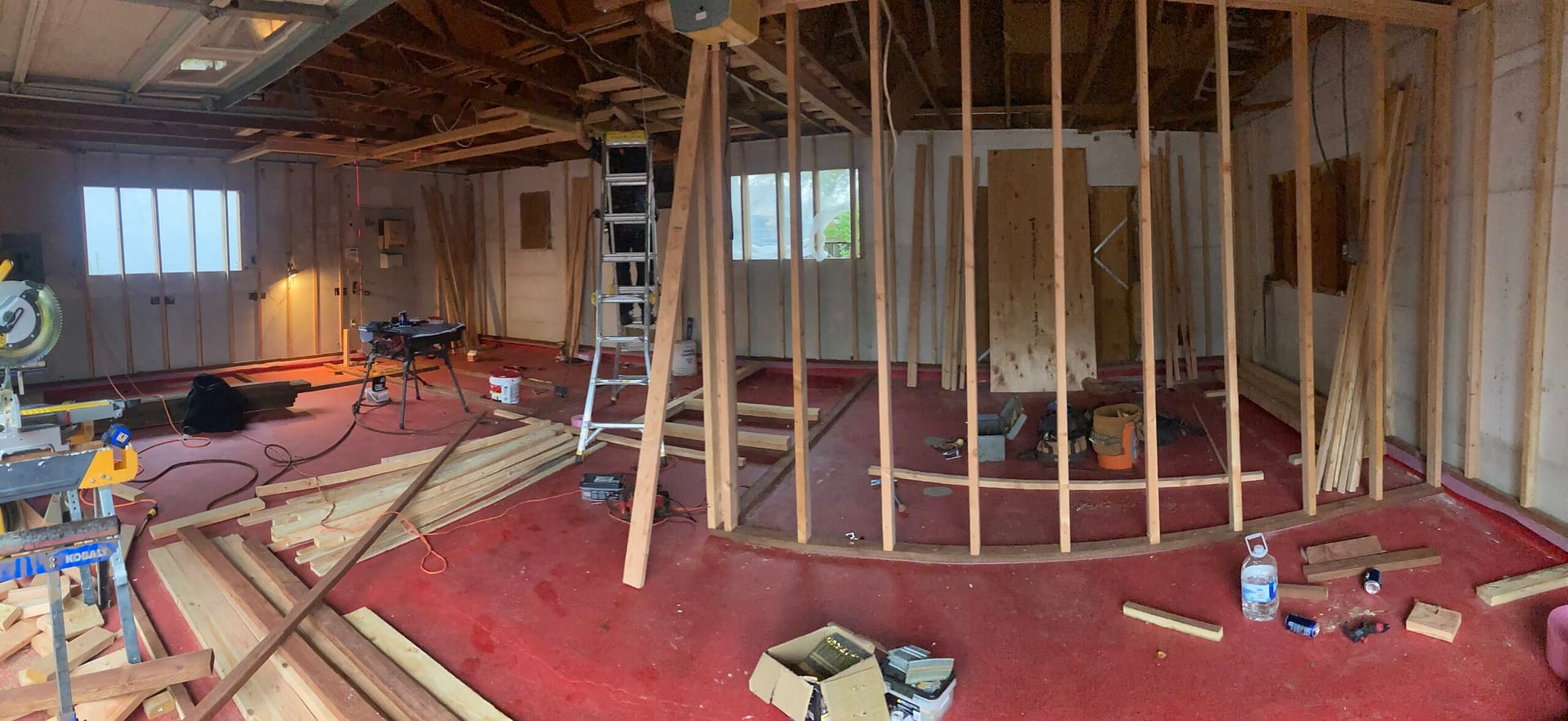 Panoramic interior view of new wood stud partition framing, exposed ceiling structure, ladders and construction tools.