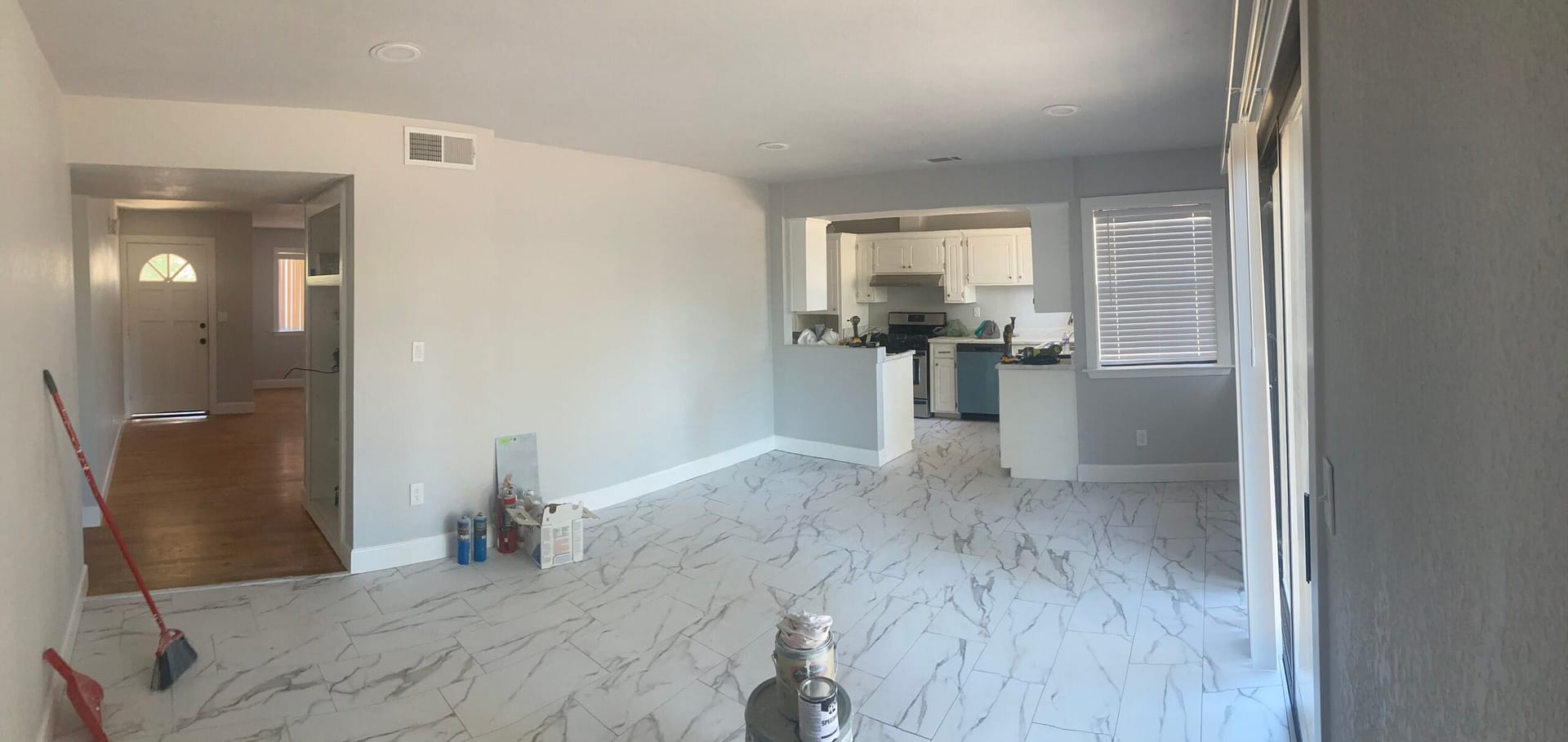 Bright living room with new-looking marble-pattern floor tile, gray walls, white baseboards and a view into the kitchen.