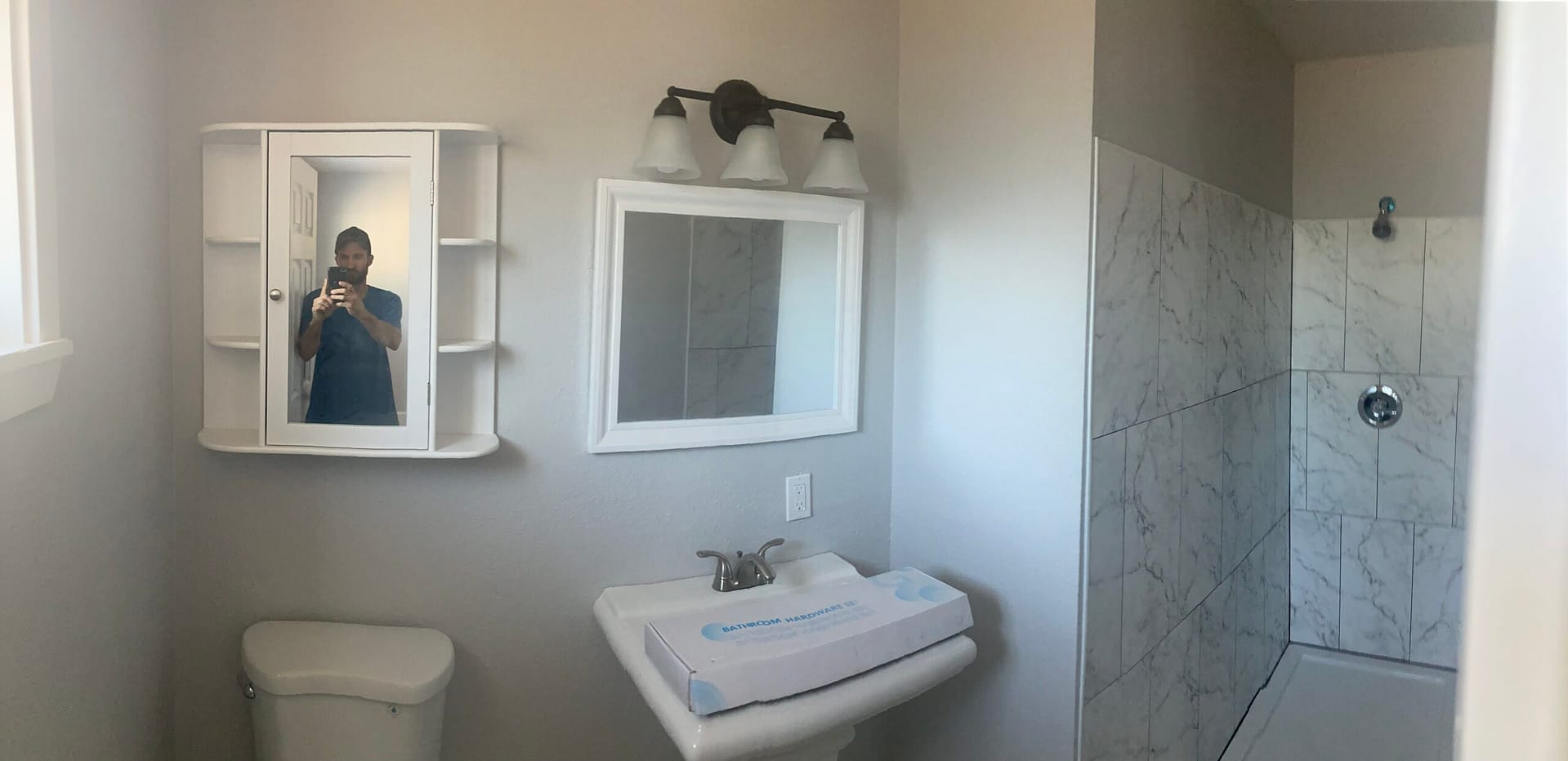 Compact bathroom with pedestal sink, medicine cabinets, wall-mounted mirrors, toilet and marble-look tiled shower.