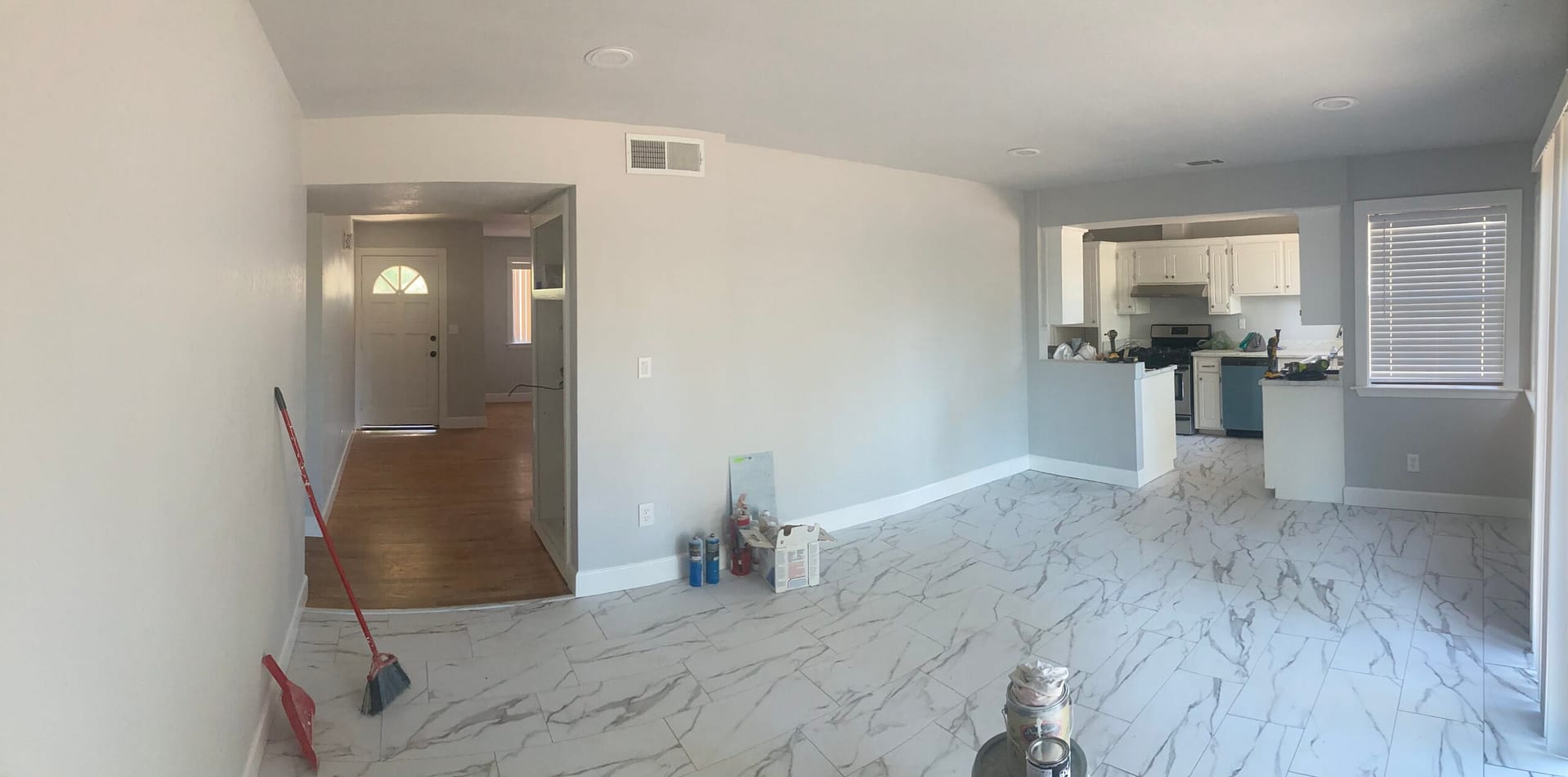 Open-plan living area with marble-look floor tile, gray walls, white baseboards and a clear view of the kitchen.