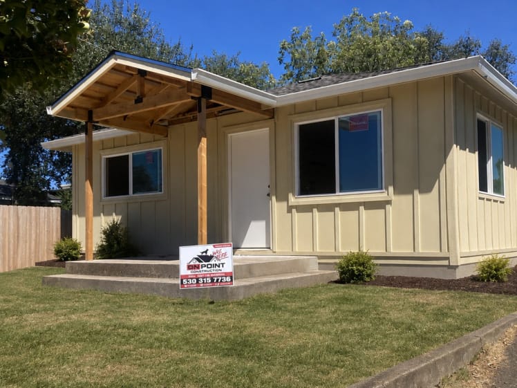Exterior home remodel before painting, with board-and-batten siding, trimmed windows and a wood-framed gabled porch cover over the front entrance.